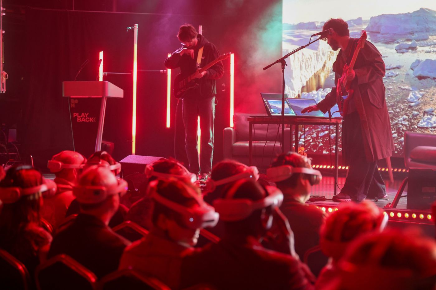 Live band performing under red light to an audience wearing VR headsets